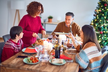 Beautiful family smiling happy and confident. One of them curving roasted turkey celebrating christmas at home