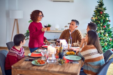 Beautiful family smiling happy and confident. One of them standing holding cup of wine speaking speech celebrating christmas at home