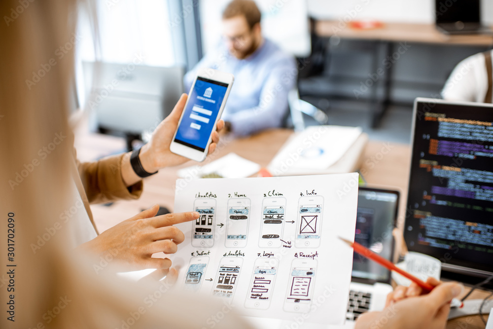 Wall mural developers or web designers developing mobile application for banking in the office, close-up on pho
