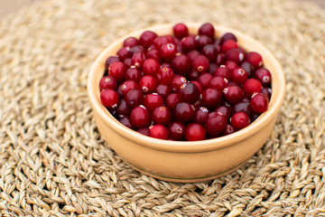 Close up red berries, cranberries in rustic bowl standing at the table in the morning in countryside during breakfast at wicker napkin