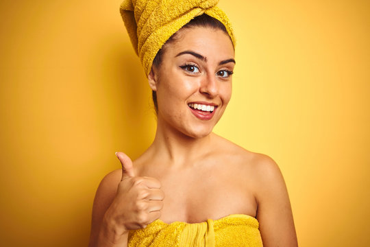 Young beautiful woman wearing towel after shower over isolated yellow background happy with big smile doing ok sign, thumb up with fingers, excellent sign