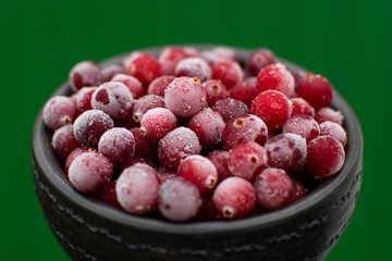 Close up winter food, frozen red berries in clay dark bowl at bright green background