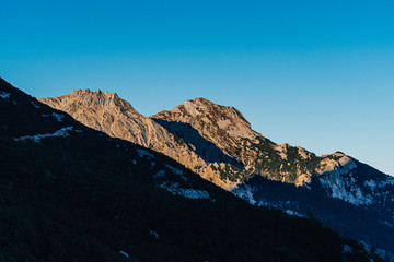 Beautiful sunset view of a mountain alpine landscape of Totes Gebirge, Austria. High alpine peaks in yellow and orange evening light. Rocky summit and rock walls of alpine peaks. Blue sky.