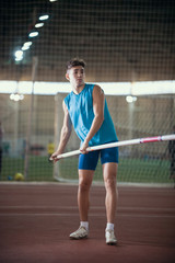 Pole vaulting - young guy in a blue suit is standing with a pole in hands