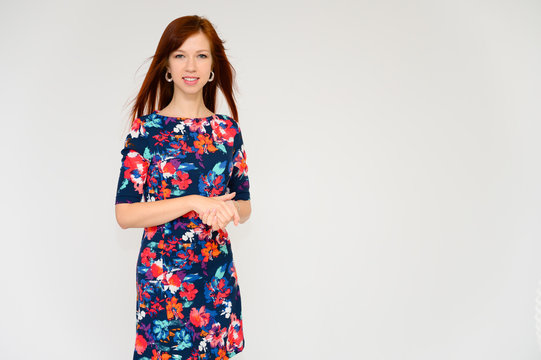Portrait of a pretty woman, red-haired student girl with long straight hair on a white background in a multi-colored dress. Talking to the camera, showing emotions, smiling.