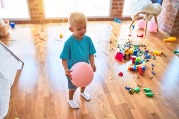 Young caucasian kid playing at kindergarten with toys. Preschooler boy happy at playroom.