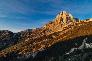 Fantastic view of a alpine mountain landscape of Totes Gebirge and the summit of Spitzmauer. Big rock wall, blue sky and mountains lid with orange sun. Sunrise or sunset mountain landscape, Austria.