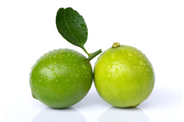 Closeup two fresh organic Lime fruits with water drops and green leaf isolated on white background .