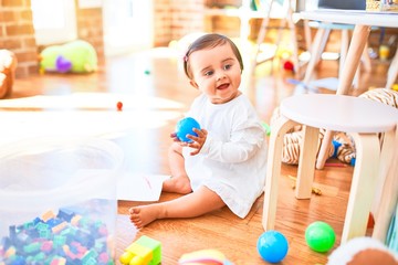 Beautiful infant happy at kindergarten around colorful toys