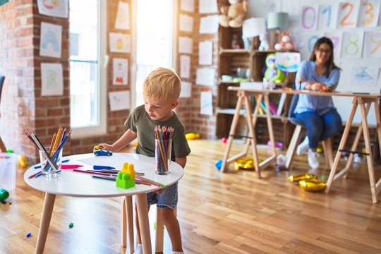 Young caucasian child playing at playschool with teacher. Young woman sitting on the desk of the classroom