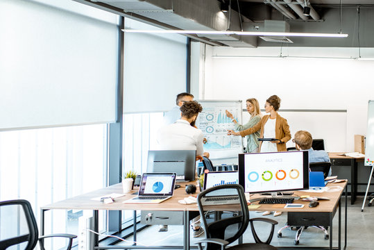 Group Of Diverse Colleagues Discussing Some Working Momets With Presentation On Flipchart During A Small Conference In The Office