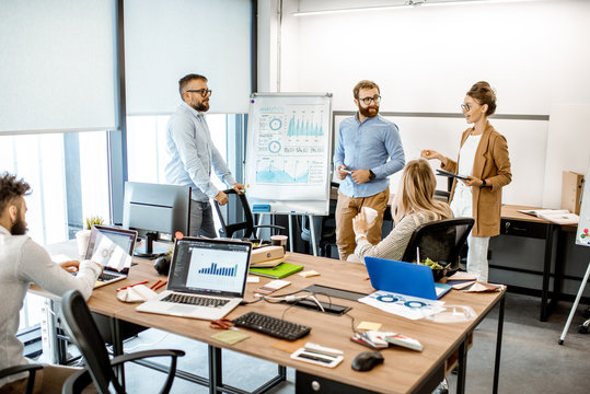 Group of diverse colleagues discussing some working momets with presentation on flipchart during a small conference in the office