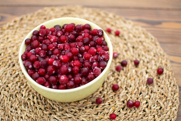 Big green bowl full of frozen cranberries with spread of red berries at wooden table at wicker napkin in the morning in countryside