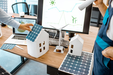 People working on a project of alternative energy, working with house model and computer in the...