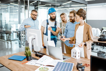Group of engineers and workman working on a project of alternative energy at the office with computer, wind turbine and solar panels model © rh2010