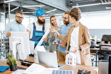 Group of engineers and workman working on a project of alternative energy at the office with computer, wind turbine and solar panels model