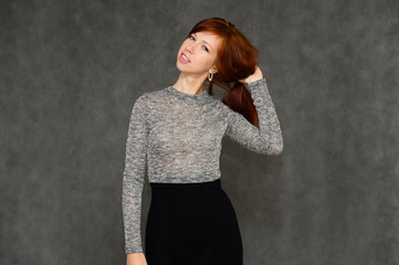 Portrait of a pretty woman, red-haired girl with long smooth hair on a gray background in a gray dress. Talking to the camera, showing joy and surprise, smiling.