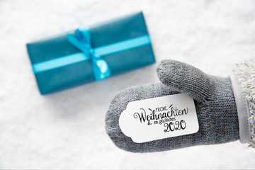 Label With German Calligraphy Frohe Weihnachten Und Ein Glueckliches 2020 Means Merry Christmas And A Happy 2020. Gray Glove With Turquoise Gift And Snow Background