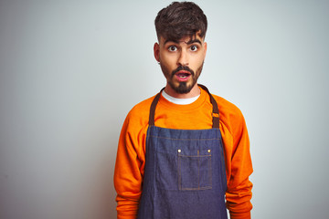 Young shopkeeper man with tattoo wearing apron standing over isolated white background afraid and shocked with surprise expression, fear and excited face.