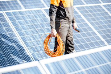 Well-equipped worker in protective orange clothing servicing solar panels on a photovoltaic rooftop plant. Concept of maintenance and installation of solar stations © rh2010