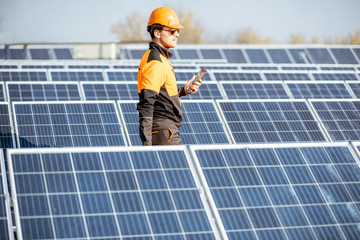 Well-equipped worker in protective orange clothing servicing solar panels on a photovoltaic rooftop plant. Concept of maintenance and installation of solar stations
