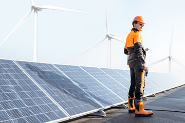Well-equipped worker in protective orange clothing examining solar panels on a photovoltaic rooftop...