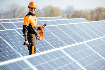 Portrait of a well-equipped worker in protective orange clothing examining solar panels on a...