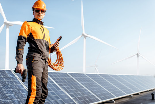 Portrait of a well-equipped worker in protective orange clothing examining solar panels on a photovoltaic rooftop plant. Concept of maintenance and installation of solar stations