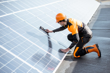 Well-equipped worker in protective orange clothing installing solar panels, measuring the angle of...