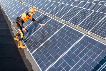 Well-equipped worker in protective orange clothing installing or replacing solar panels on a...