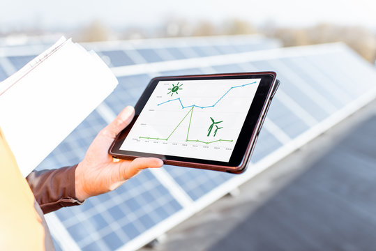 Man with digital tablet on a solar station, close-up on a tablet screen with a chart of solar and wind power daily generation. Concept of online monitoring of the electric station