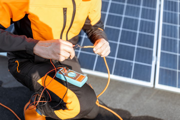 Well-equipped electrician connecting solar panels, checking the voltage and connecting wiring on a rooftop photovoltaic power plant