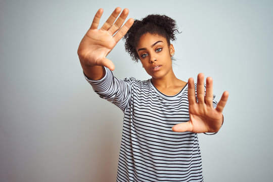 African american woman wearing navy striped t-shirt standing over isolated white background doing frame using hands palms and fingers, camera perspective