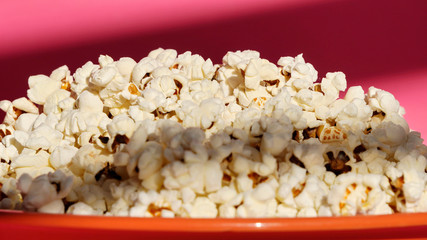coral plate with popcorn on the table on a pink background. a snack, a treat to the cinema or the circus. exploding corn kernels.