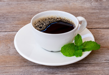 Closeup white cup of hot black coffee with mint leaf isolated on rustic wooden table background. Vintage style. 