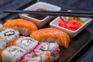 Japanese sushi and rolls with soy sauce and ginger. On a black rustic background