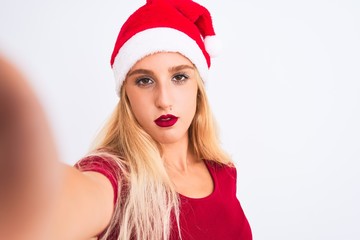 Woman wearing Christmas Santa hat make selfie by camera over isolated white background with a confident expression on smart face thinking serious