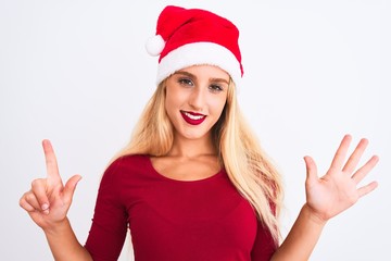 Young beautiful woman wearing Christmas Santa hat over isolated white background showing and pointing up with fingers number seven while smiling confident and happy.