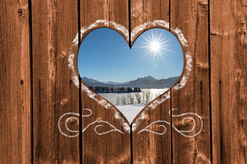 Looking through a carved heart in a wooden wall to beautiful snow covered landscape