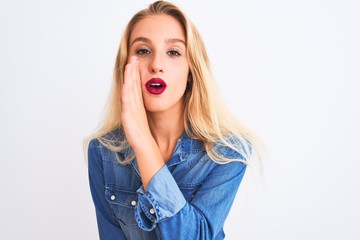 Young beautiful woman wearing casual denim shirt standing over isolated white background hand on mouth telling secret rumor, whispering malicious talk conversation