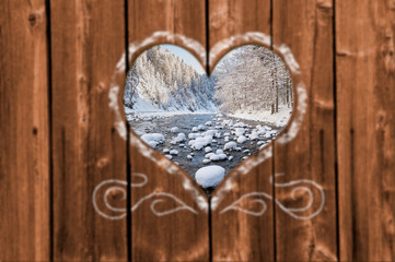 Looking through a carved heart in a wooden wall to an frozen wild river in Bavaria