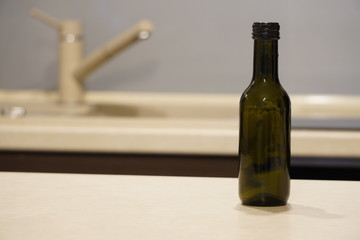 Obraz na płótnie Canvas a small dark glass wine bottle stands on the table against the kitchen background. decor, home decoration.