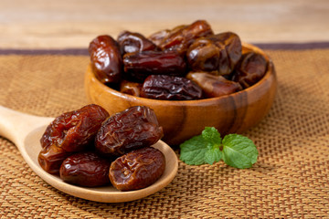 Fototapeta na wymiar Closeup date palm fruits in wooden bowl and spoon with mint green leaf isolated on wood table background.