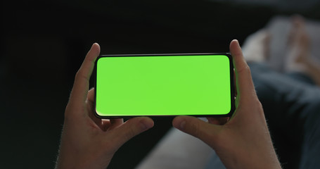 man hold smartphone with green screen while lying on a couch