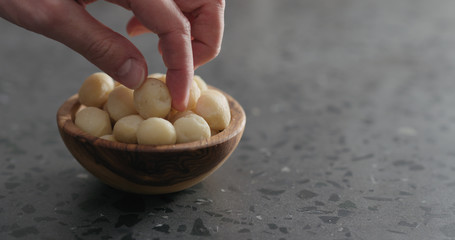 man hand take peeled macadamia nut from olive wood bowl