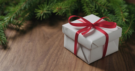 white gift box with red ribbon near spruce twig on walnut table