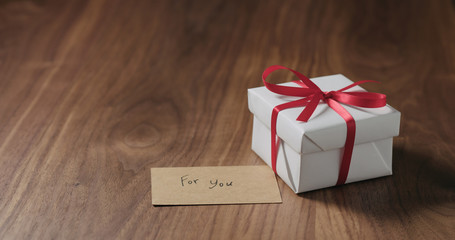 white gift box with red ribbon and for you card on walnut table