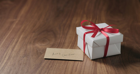 white gift box with red ribbon and mett christmas card on walnut table