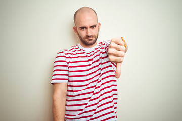 Naklejka premium Young bald man with beard wearing casual striped red t-shirt over white isolated background looking unhappy and angry showing rejection and negative with thumbs down gesture. Bad expression.