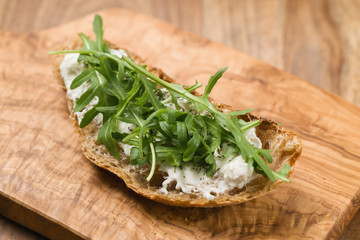 crunchy rustic bread with ricotta and arugula on olive wood board